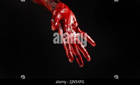 Nahaufnahme einer mit Blut befleckten männlichen Hand auf schwarzem Hintergrund. Stockfoto