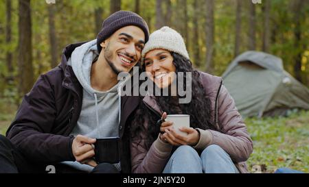 Glückliches Ehepaar trinkt im Herbstwald heißes Getränk Junge Wanderer ruhen sich in der Natur auf dem Campingplatz aus Verliebte kommunizieren unbeschwert genießen Stockfoto