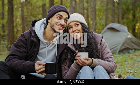 Glückliches Ehepaar trinkt im Herbstwald heißes Getränk Junge Wanderer ruhen sich in der Natur auf dem Campingplatz aus Verliebte kommunizieren unbeschwert genießen Stockfoto