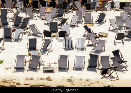 Landschaftlich schöner Blick auf das Wasser von vielen leeren schwarzen Holzliegen auf dem Sandfluss oder dem Meeresstrand. Reihen von Liegestühlen an geschlossener Küste aufgrund von Kontamination Stockfoto