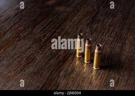 Eine Nahaufnahme von drei leeren Geschossgehäusen auf einem dunklen Holztisch Stockfoto