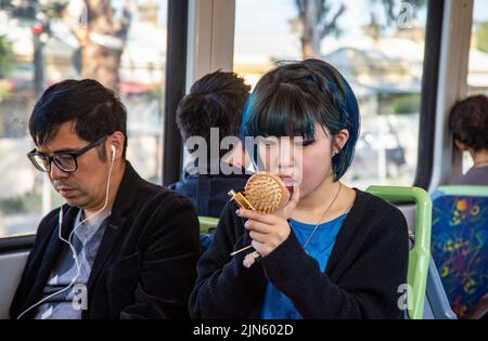 Eine asiatische Büroangestellte schminkt sich im Zug, während sie zur Arbeit in Melbourne, Australien, pendelt Stockfoto