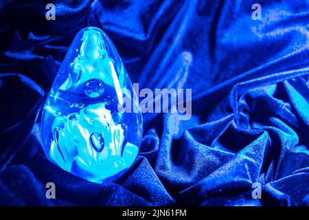 Nahaufnahme einer blau-violetten eiförmigen Glaskugel auf dem blau-violetten Samttuch Stockfoto