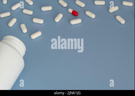 Vitamine Tabletten Ergänzungen kommen aus der Flasche mit einer roten und weißen Pille auf blauem Hintergrund. Platz zum Schreiben unten rechts. Stockfoto