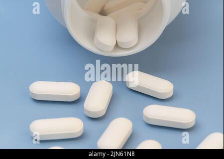 Vitamine Tabletten Ergänzungen Medizin kommt aus der Flasche auf blauem Hintergrund. Stockfoto