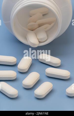 Vitamine Tabletten Ergänzungen Medizin kommt aus der Flasche auf blauem Hintergrund. Stockfoto