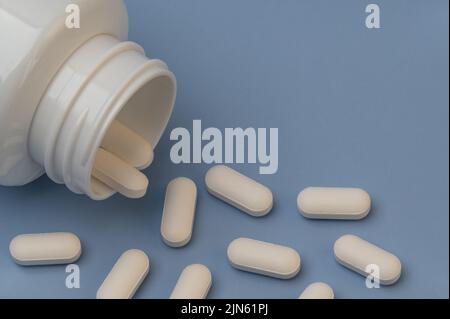 Vitamine Tabletten ergänzt Medikamente kommen aus der Flasche auf blauem Hintergrund. Stockfoto