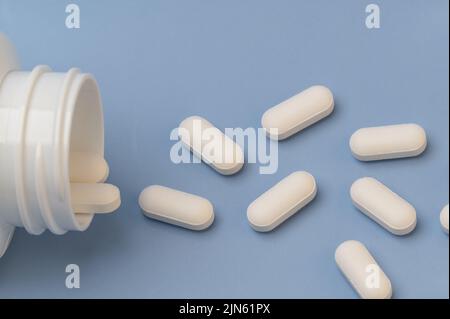 Vitamine Tabletten ergänzt Medikamente kommen aus der Flasche auf blauem Hintergrund Stockfoto