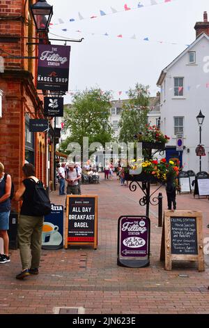 Ein Blick entlang der Old Fore Street im Stadtzentrum von Sidmouth, wo die Menschen in den Geschäften stöbern und farbenfrohe Blumenvorführungen zeigen. Stockfoto