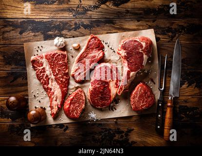 Sammlung von rohem Fleisch. Steak, Knochensteak und Filetmedaillon auf rustikalem Holzhintergrund Stockfoto