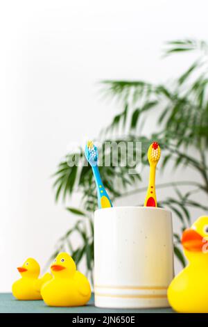 Helle Kinderzahnbürsten in einer Tasse, gelbe Gummienten, Pflege für Kinderzähne Stockfoto