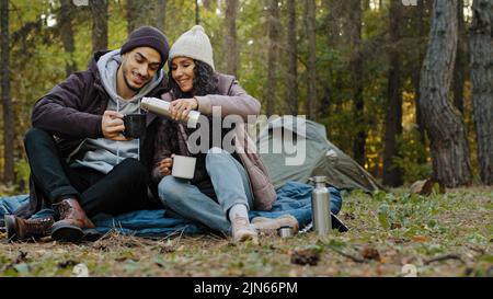 Junges Paar in der Liebe Reisende sitzt in der Natur ruhen trinken Tee aus Thermoskannen genießen heißes Getränk ruhen Gespräch lächelnd Lachen fühlen Vergnügen reisen Stockfoto