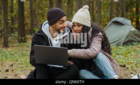 Junge glückliche Paar in der Liebe Touristen sitzen im Freien auf dem Campingplatz Blick auf Laptop-Bildschirm wählen Ort auf der elektronischen Karte reisen Verwenden Sie Computer-Anwendung Stockfoto