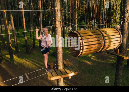 Eine Frau überwindet ein Hindernis in einer Seilstadt. Eine Frau in einem Waldseilpark. Stockfoto