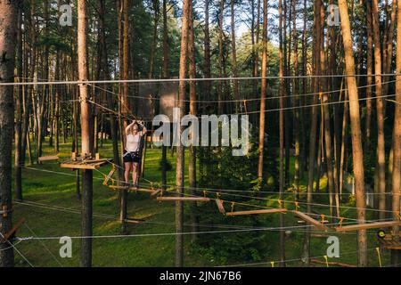 Eine Frau überwindet ein Hindernis in einer Seilstadt. Eine Frau in einem Waldseilpark. Stockfoto