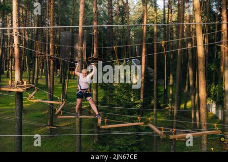 Eine Frau überwindet ein Hindernis in einer Seilstadt. Eine Frau in einem Waldseilpark. Stockfoto