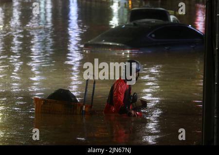 SEOUL, 9. August 2022 (Xinhua) -- Ein Fahrer schiebt ein Motorrad auf einer überfluteten Straße im Gangnam-Bezirk von Seoul, Südkorea, 8. August 2022. Acht Menschen wurden getötet und sechs weitere wurden vermisst, als die südkoreanische Metropolregion von schweren Regenfällen heimgesucht wurde, teilte das zentrale Hauptquartier für Katastrophenschutz und Gegenmaßnahmen am Dienstag mit. Über 100 Millimeter Regen pro Stunde trafen am Montagabend in der Hauptstadt Seoul, der westlichen Hafenstadt Incheon und der Provinz Gyeonggi, die Seoul umgibt, ein. (NEWSIS über Xinhua) Stockfoto