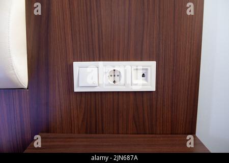 Eine Nahaufnahme einer weißen Steckdose, eines Netzsteckers und eines Lichtschalters an einer Holzpaneelwand. Stockfoto