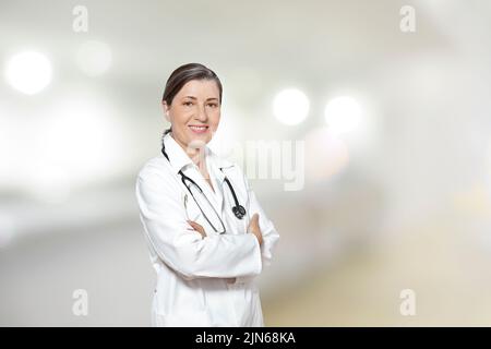 Ärztin mittleren Alters in einem weißen Laborkittel, lächelnd freundlich, in ihrer Praxis oder Operation, Kopie oder Textraum. Stockfoto