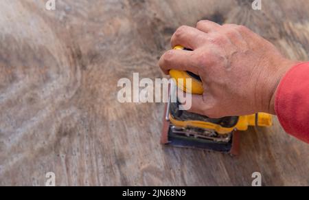 Die Hand eines Mannes mit elektrischem Schleifer auf einem hölzernen Hintergrund macht Arbeit Stockfoto