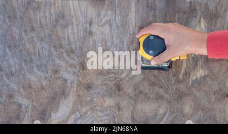 Übersichtsfoto einer Männerhand mit einem elektrischen Schleifer auf einer Holzplatte, die Restaurierungs- oder Schreinerei-Arbeiten durchführt Stockfoto