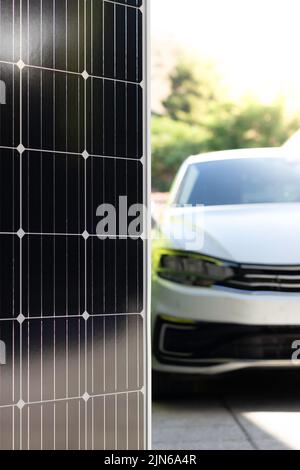 Vertikale Ansicht des verschwommenen modernen weißen Elektroautos mit Solarmodulen im Fokus als Konzept für erneuerbare Energien Stockfoto