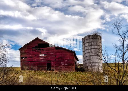 Verwitterte Scheune und Silo mit blauem bewölktem Himmel auf einem Hügel Stockfoto