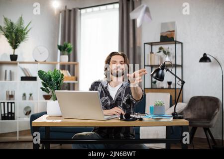 Lächelnder freier Mann, der mit dem Papierflugzeug spielt, während er von zu Hause aus arbeitet. Attraktiver kaukasischer Mann, der während der Arbeitszeit Pause macht. Stockfoto