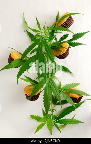 Ein Zweig von Cannabis, auf dem fünf Marihuana-Muffins angebaut wurden. Glutenfrei. Das Konzept der alternativen Süßigkeiten. Vertikale Ausrichtung. Draufsicht Stockfoto