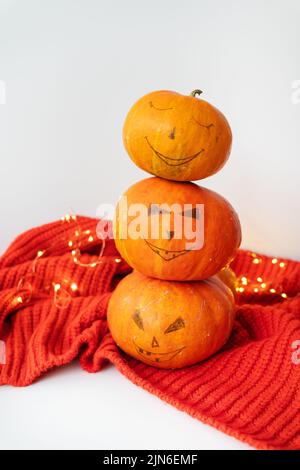 Drei Kürbisse mit einem bemalten Gesicht auf einem roten Pullover. Das Konzept des Feiertages am 31. Oktober, Halloween. Schönes Bokeh im Hintergrund Stockfoto