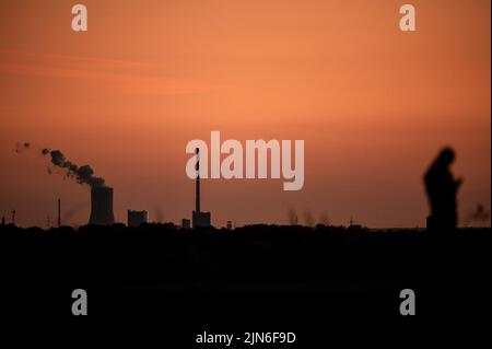 Bottrop, Deutschland. 08. August 2022. Das Kraftwerk Steag in Duisburg Walsum ist bei Sonnenuntergang zu sehen, während eine Person im Vordergrund auf dem Tetraeder-Schlackenhaufen läuft. Quelle: Fabian Strauch/dpa/Alamy Live News Stockfoto