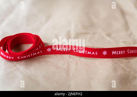 Rotes Band mit der Aufschrift Frohe Weihnachten auf Bastelpapier verteilt. Platz für eine Inschrift Stockfoto