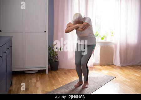 Ältere Frau trainiert drinnen, dehnt Muskeln aus. Stockfoto