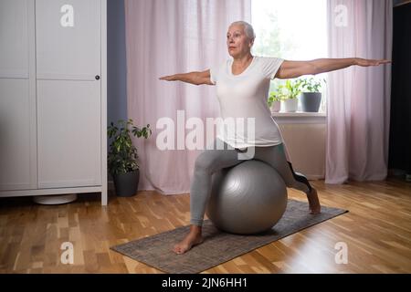 Ältere Dame, die Yoga Asana im Wohnzimmer macht. Stockfoto