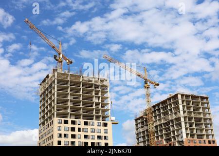 Zwei Turmdrehkrane und unfertige Gebäude auf dem Hintergrund des blauen Himmels mit weißen Wolken. Wohnungsbau, Wohnblocks in der Stadt Stockfoto