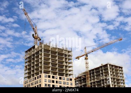 Zwei Turmdrehkrane und unfertige Gebäude auf dem Hintergrund des blauen Himmels mit weißen Wolken. Wohnungsbau, Wohnblocks in der Stadt Stockfoto