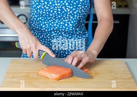 Frau schneidet frisches Lachsfilet auf Holzbrett Stockfoto