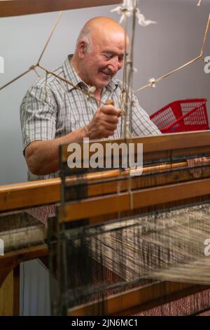 Ardara, Irland - 13. Juli 2022: Meisterin bei der Arbeit an einem traditionellen Holzwebstuhl und der Handweberei von Wollheringbone Stockfoto
