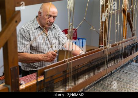 Ardara, Irland - 13. Juli 2022: Meisterin bei der Arbeit an einem traditionellen Holzwebstuhl und der Handweberei von Wollheringbone Stockfoto