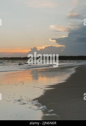 Teilweise bewölkter Sonnenuntergang an der Küste von North Carolina, USA, wo Wasser auf den Sand trifft Stockfoto