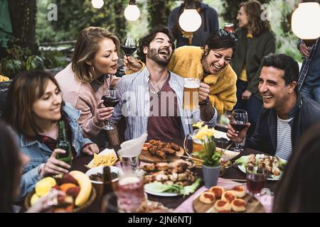 Eine Gruppe von urkomischen Freunden aus verschiedenen Rassen hat am Wochenende Spaß, Bier und Wein zu trinken und gemeinsam am Restauranttisch auf dem Land zu essen Stockfoto