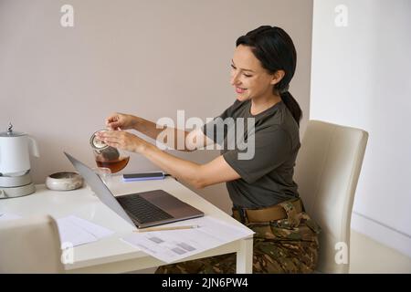 Frau in Tarnkleidung gießt sich Tee Stockfoto