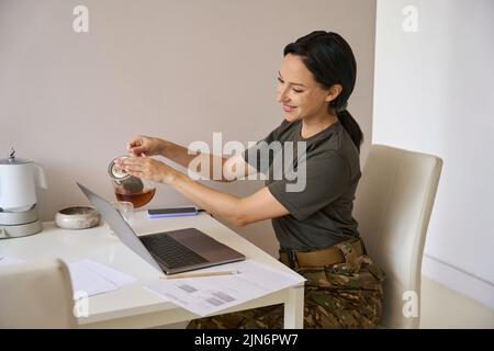 Frau in Tarnkleidung gießt sich Tee Stockfoto