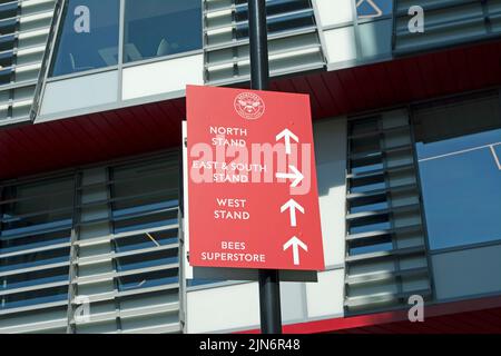 Richtungsschild in Vereinsfarben vor dem Stadion des fußballvereins brentford, das derzeit als gtech-Gemeinschaftsstadion, brentford, london, england, bezeichnet wird Stockfoto