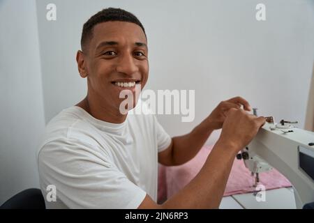 Glücklicher junger Mann, der mit der Nähmaschine arbeitet Stockfoto