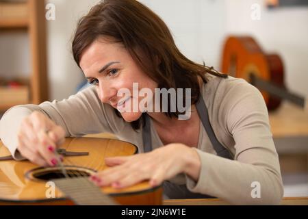 Frau, die in der Werkstatt einen Gitarrenhals in Holz schleift Stockfoto