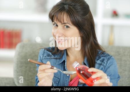 Glückliche Frau, die zu Hause eine flüssige Medizin trinkt Stockfoto