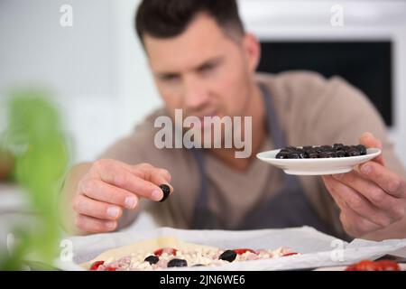 Mann, der Oliven als Pizza-Belag hinzufügte Stockfoto