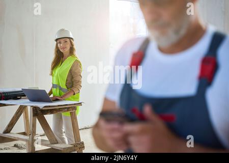 Zugeschnittenes Foto des Baumeisters in Overalls beim Eintippen einer Nachricht auf dem Handy Stockfoto