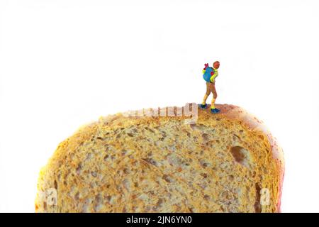 Ein Wanderer mit Rucksack steht auf einer Scheibe getoastetes Brot, weißer Hintergrund Stockfoto